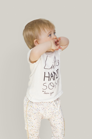 little girl with blue eyes on a grey background covers his face with his handsの写真素材
