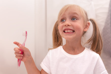 Happy child girl brushing teeth in the bathroom with a toothbrush. Looks in the mirror and smilesの写真素材