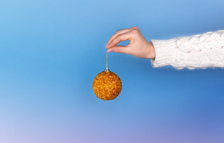 on a blue background close-up the hand of a European girl in a white knitted sweater holds a New...