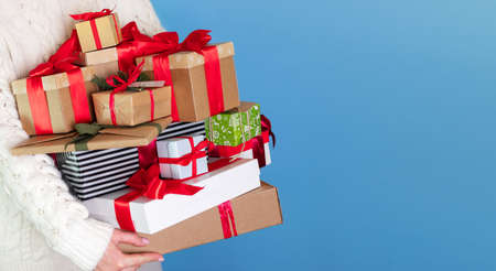 girl in white sweater holds many gifts in her hands close-up. The boxes, large and small, are...