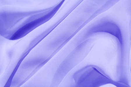 The soft fabric is lined with beautiful deep folds that catch cold light. Abstract art background in trending colors of 2022. The color of Veri Peri.の写真素材