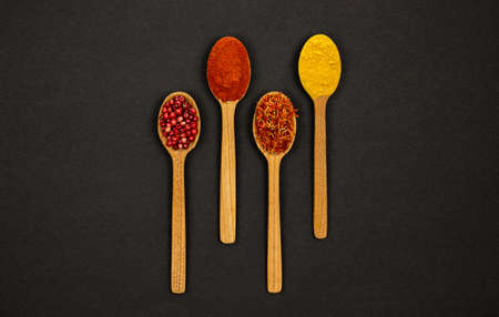 Set. On a black background, in the central part, there are four wooden spoons with spices, bell...