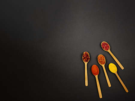 Kit. On a black background, to the right of the center, there are four wooden spoons filled with spices, bell pepper, chili, turmeric and peppercorn. Copy and paste the space around.の写真素材