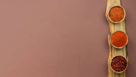 On a wooden beautiful cutting, serving board, three bowls with hot oriental spices: saffron, pepper...