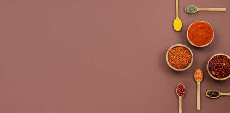 five spoons and three wooden bowls with fragrant oriental spices are placed on a brown background....