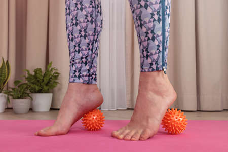 A woman in Veri Perry sportswear on a pink yoga mat makes foot massage at home with special prickly...