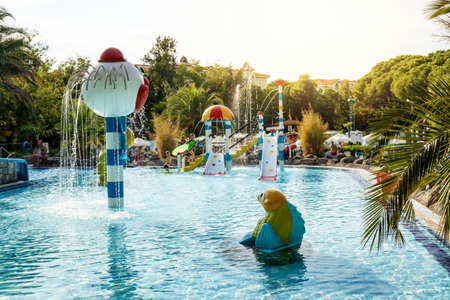 Outdoor water park, pool for small children with fountains and water slides. Sunny day and green...