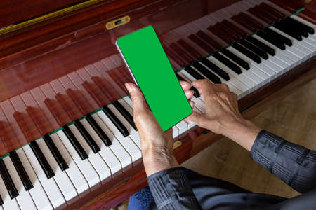 old woman plays the piano, looks into the phone notes. Chroma key on smartphone