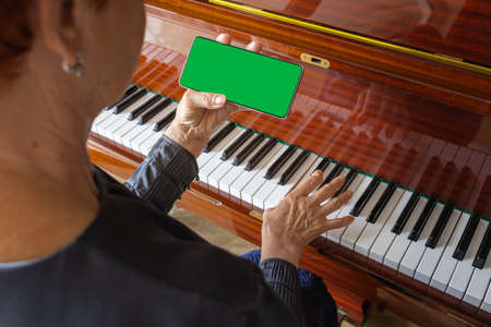 old woman plays the piano, looks into the phone notes. Chroma key on smartphone