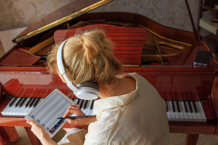 a young girl composes music near the piano and writes into the program on tablet