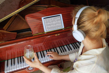 A girl with a glass of wine is sitting near the piano. The concept of lonelinessの写真素材