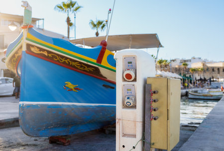 A traditional blue Maltese boat, with eyes, is charging its battery on the pierの写真素材