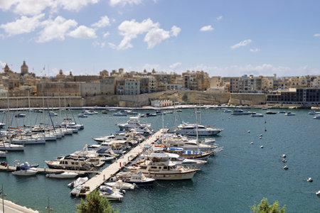 Scenic marina with yachts and boats, historic city walls, and Mediterranean architecture under blue sky.の写真素材