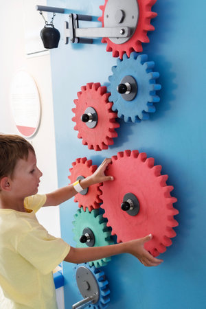 Child interacting with colorful gears on a mechanical wall, exploring engineering concepts in a museum.の写真素材