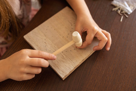 Close-up of a child hands using a hammer on wood. Crafting, learning, and building patienceの写真素材