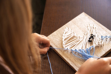 Child weaving string art on wood. Developing patience, creativity, and fine motor skills through crafting.の写真素材