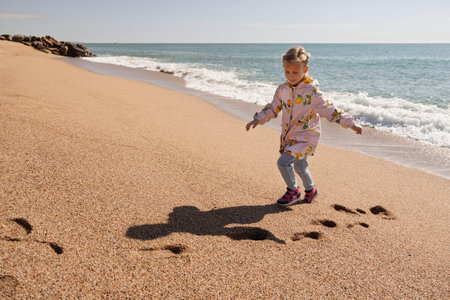 Girl runs on a sandy beach by the sea in warm clothes. Winter in Spain. Fresh air, freedom, and joyの写真素材