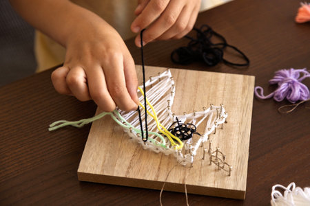 Child carefully wraps thread around tiny nails, building patience, focus, and artistic skills.の写真素材
