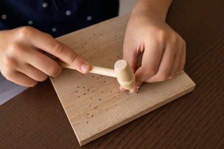 Child hands hammering nails into wood. Developing creativity, patience, and fine motor skills through crafting.の写真素材