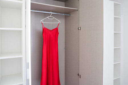 Red dress on hanger in open wardrobe with shelves, simple clean closet in modern bright room.の写真素材