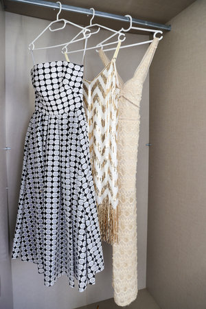Close-up of three elegant dresses hanging on white hangers inside a modern open wardrobe.の写真素材