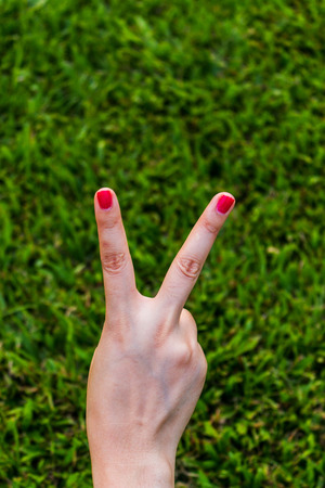 Woman hand holding up the peace sign or number two with two fingers on green grass background textureの写真素材