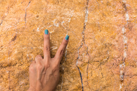 Woman hand holding up the peace sign or number two with two fingers on stone background textureの写真素材