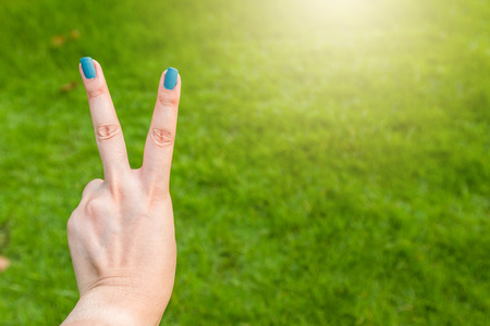 Women hold two fingers on green grass background textureの写真素材