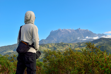 Unrecognized man on white hooded long sleeve shirt and sling bag, appreciating the beauty of nature at Bundu Tuhan, Ranau, Sabah, Malaysia in one early morning. Seen at far is the majestic Mount Kinabalu.のeditorial素材