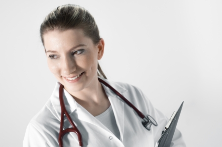 Young female doctor with stethoscope and board smiling, watching camera leftの写真素材
