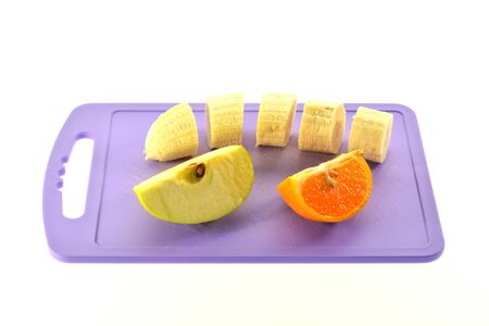banana slices of apple and mandarin on purple chopping boardの写真素材