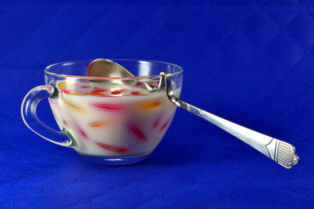 Multicolored marmalade and a cup of milk with a spoon on a blue backgroundの写真素材