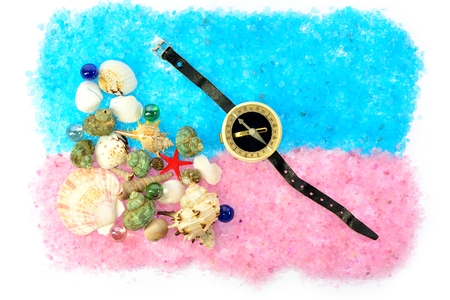 sea shells and a compass with a black strap on blue and pink saltの写真素材