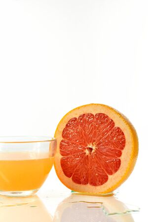 Sliced half of a ripe grapefruit and a glass of juice on a white backgroundの写真素材