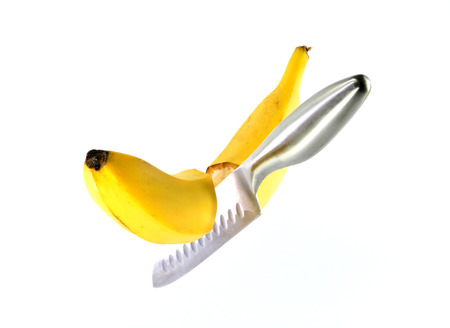 Steel knife cuts ripe banana on a white backgroundの写真素材