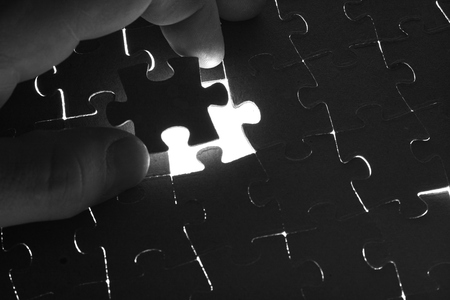Hand lays black puzzle on a white backgroundの写真素材