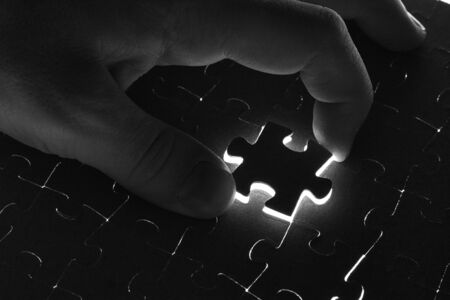 Hand lays black puzzle on a white backgroundの写真素材