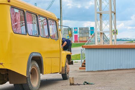 A man in a blue shirt repairs yellow busの写真素材