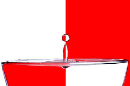 A drop of water falls in a glass of red on a white backgroundの写真素材