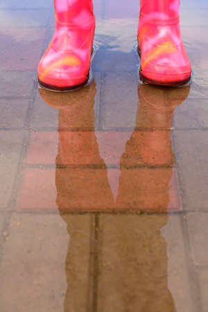 The girl in pink boots jumping in puddles after rainの写真素材