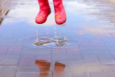 The girl in pink boots jumping in puddles after rain