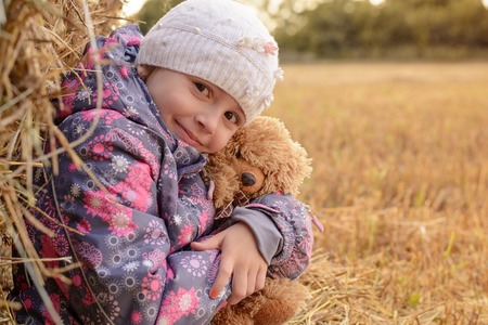 The girl with a soft toy around haystacks autumn