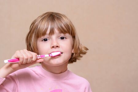 Girl brushing her teeth pink toothbrush on a light background