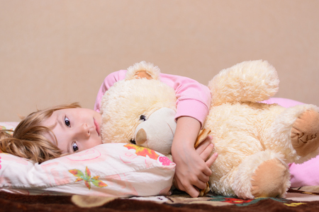 Girl lying on the bed hugging teddy bearの写真素材