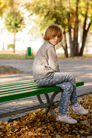 Sad girl sitting on a bench in the park in autumnの写真素材