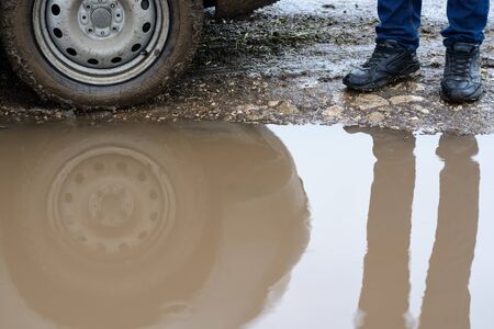 Reflection wheel car in a muddy puddle and men's feet in shoes