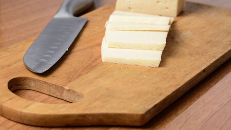 Cut cheese on a wooden board and knifeの写真素材