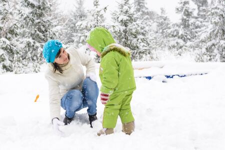 Little baby and mother are playing with first snow in the playgroundの写真素材