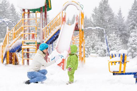 Little baby and mother are playing with first snow in the playgroundの写真素材