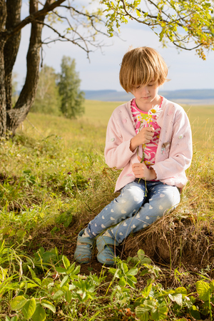 The girl with short blond hair sitting on the grass in the summerの写真素材